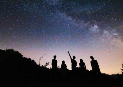 Silhouettes d'enfants regardant la voie lactée et pointant du doigt une étoile lors d'une initiation à l'astronomie en Cévennes