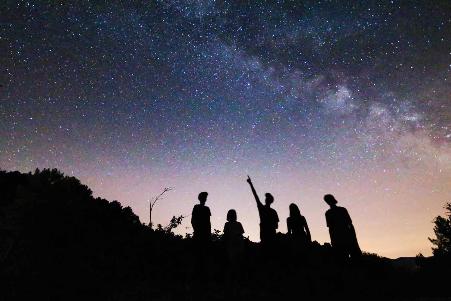 Silhouettes d'enfants regardant la voie lactée et pointant du doigt une étoile lors d'une initiation à l'astronomie en Cévennes