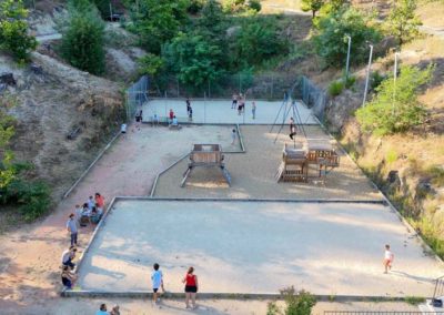 Grand terrain de jeux au soleil couchant avec des terrains de pétanque au prmeier plan, des aires de jeux et une balonçoire en suivant et en fond un mini foot. Le tout entourée par la nature des Cévennes