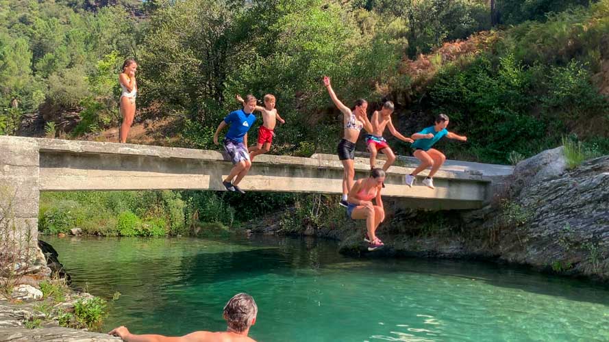 Enfants et adolescents sautent d'un petit pont dans la rivière bleu turquoise