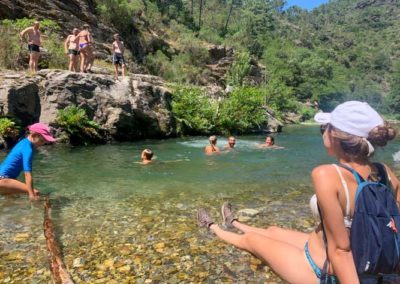 Après midi typique de randonnée aquatique, les ados sautent d'un rocher, les parents nagent dans l'eau transparente et les enfants jouent avec des batons sur le bord de l'eau