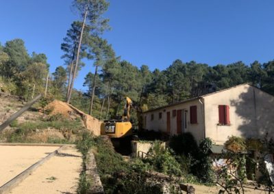 Pelle mécanique au travail au ras du bâtiment d'accueil du village de gîtes de Ravel en Cévennes