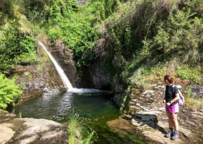 Jeune femme en tenue de randonnée regarde une cascade tomber dans une large vasque de schiste cévenol.