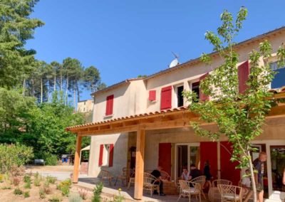 Terrasse avec charpente en bois douglas ombragée devant un mas méridional du village de gîtes de ravel en cévennes. Les volet rouge donnent un coté vivant et chaleureux